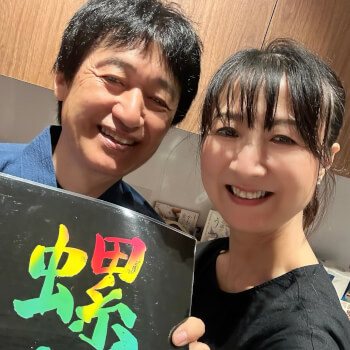 Akki and Hisae smiling, holding a raden sign